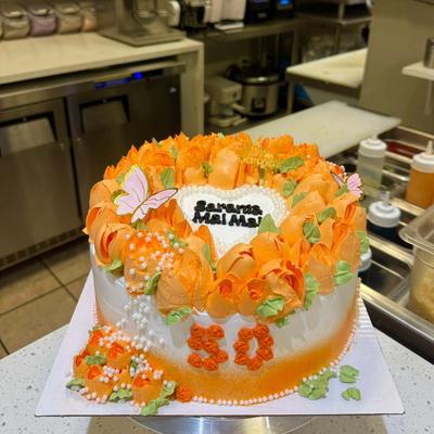 Orange buttercream floral cake decorated with edible pearls, butterflies, and a heart plaque.