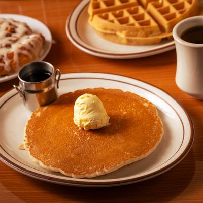 Pancake topped with a pat of butter, served with syrup, a waffle, and coffee.