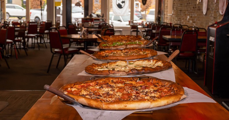 Row of freshly baked pizzas lined up on a wooden counter