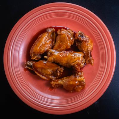 Overhead view of BBQ chicken wings on a red plate.