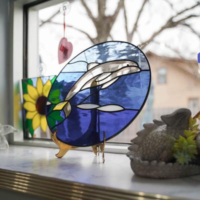 A colorful stained glass dolphin art piece by the window.