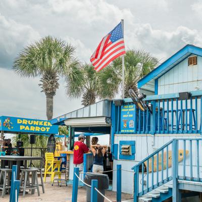 Blue restaurant exterior with outdoor seating, an American flag and palm trees.