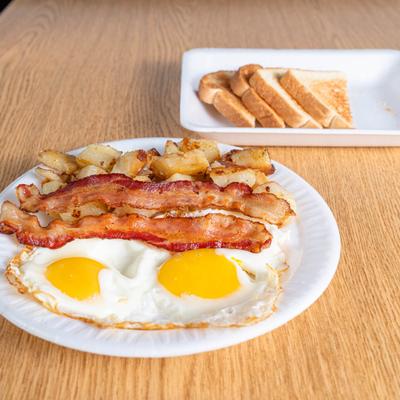 Two sunny-side-up eggs with crispy bacon, home fries, and toasted bread.