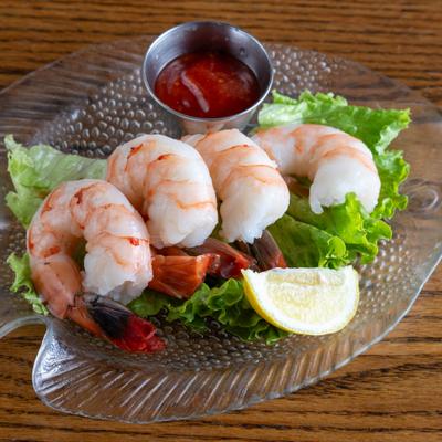 Jumbo shrimp cocktail served on lettuce with a side of sauce and a lemon wedge.