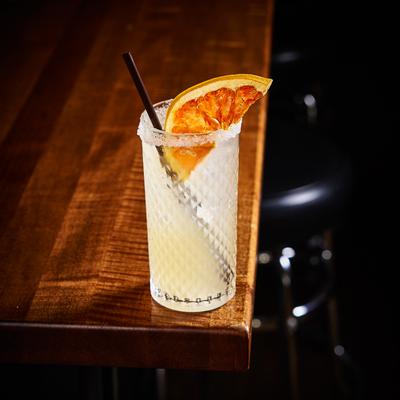 Paloma cocktail served in a salt-rimmed highball, garnished with dried grapefruit.