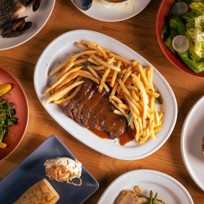 Streak and frites surrounded by various other dishes, overhead view.