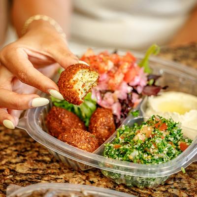A hand holding a half-eaten falafel over a falafel platter.