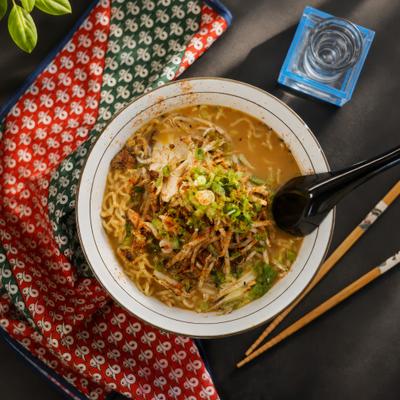 A bowl of ramen noodle soup served with chopsticks and a spoon.