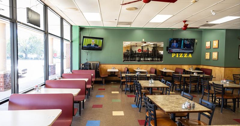 Interior of a spacious pizza restaurant with booths, tables, ceiling fans, televisions