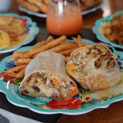 Breakfast burrito and fries, with other dished and a grapefruit mimosa in the background.
