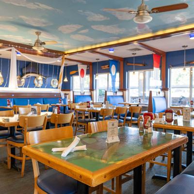 Interior with wooden tables, blue booths, sky-painted ceiling, and nautical-themed decor.
