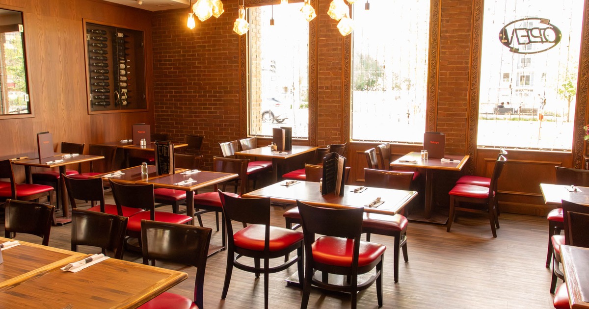 Interior of a restaurant with wooden tables, red-cushioned chairs, large windows and a wine rack