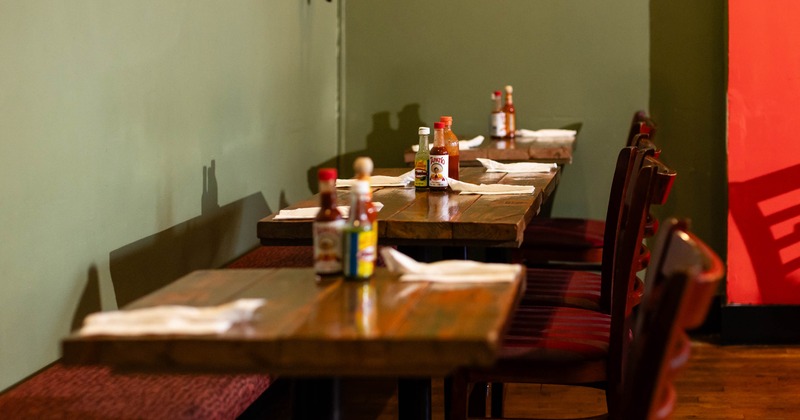 Row of wooden tables in a restaurant with sauce bottles and napkins