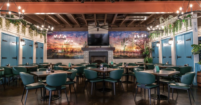 Interior, dining room with teal chairs, turquoise doors, hanging plants, central fireplace, mural