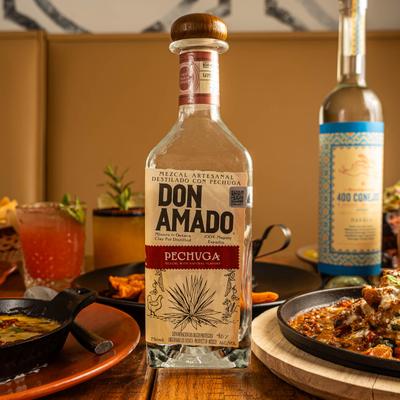 Mezcal bottle with assorted food plates on a table.