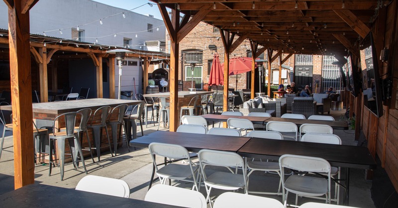 Exterior, seating area, wooden structure, various tables and chairs, red umbrellas, string lights