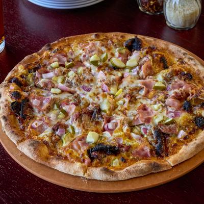 Pizza topped with ham, bacon, pulled pork, and pickles.
