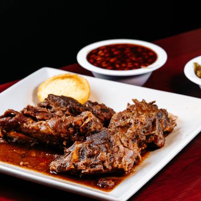Braised pork shoulder in sauce with cornbread and a side of baked beans.