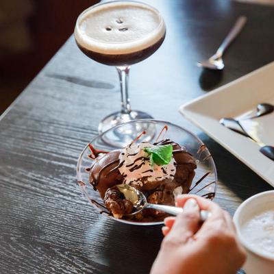 A person enjoying Profiterole with a glass of Espresso Martini.