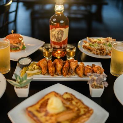 Smoked wings with pickled celery surrounded by Parmesan fries, French toast, burger, and drinks.