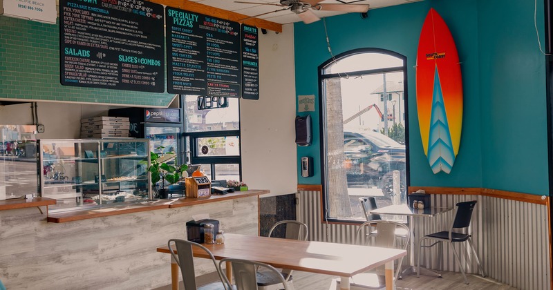 Order counter, tables for dining, and a surfboard on the wall