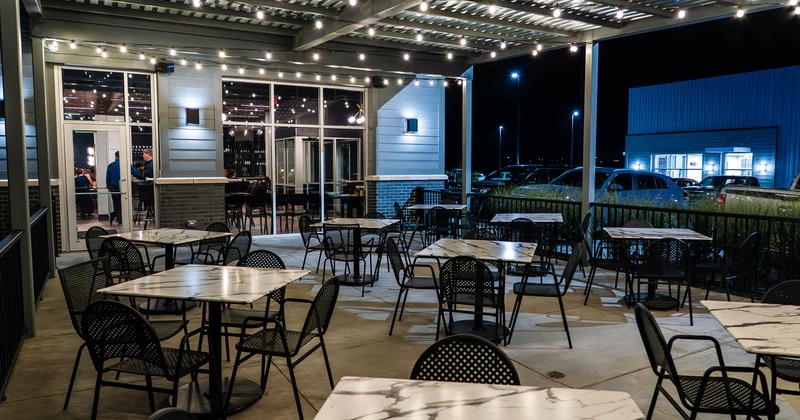 Outdoor restaurant patio at night with string lights, tables and chairs.