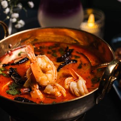 Tom yum soup in a copper pot with shrimp, chilies, and fresh herbs.