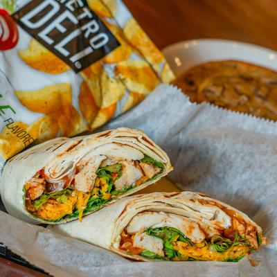 Grilled chicken wrap beside a bag of spicy pickle dill potato chips.