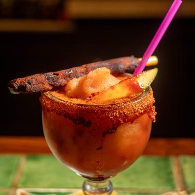 Mangonada frozen drink with tamarind stick and mango slice garnish.