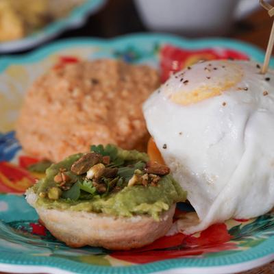 A colorful plate featuring a fried egg, a biscuit topped with guacamole and nuts, and grits.