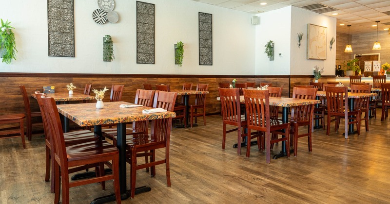 Cozy restaurant interior with wooden tables and chairs, wall art, and plants
