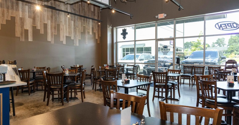 Interior, open space dining area, wooden tables with chairs, entrance and large shop windows