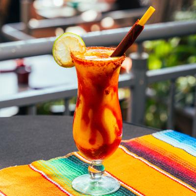 Mangonada drink served in a hurricane glass with chili salt rim, lime wheel, and tamarind stick.