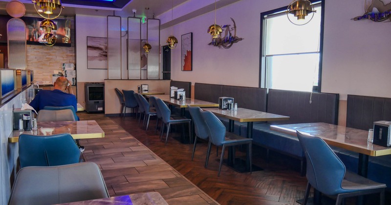 Modern restaurant dining room with blue and gray seating, brass pendant lights, abstract wall art