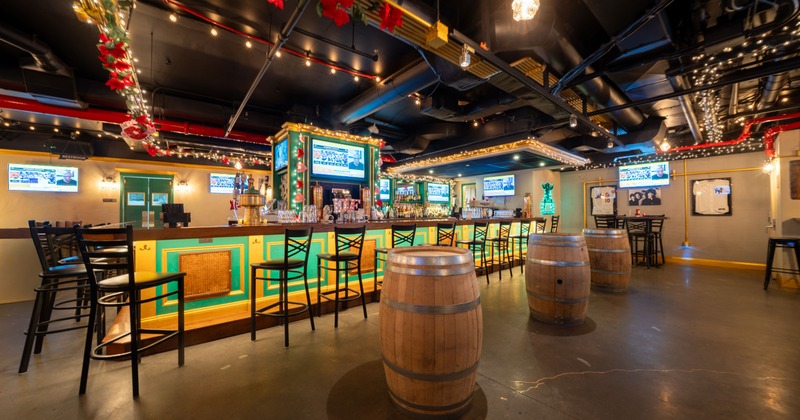 Interior of a stylish and cozy sports bar with a large bar and wooden barrels as standing tables