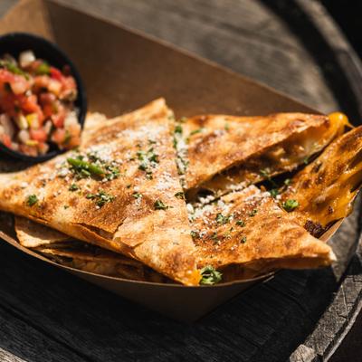 Chicken quesadilla topped with herbs and grated cheese, served with salsa.