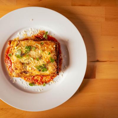 Lasagna Bolognese on white plate with sauce, overhead view.