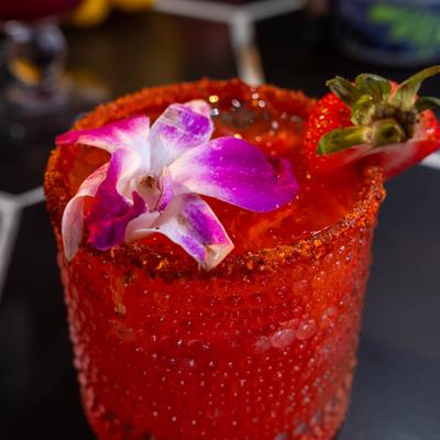 Strawberry mezcal margarita garnished with a strawberry and a purple orchid.