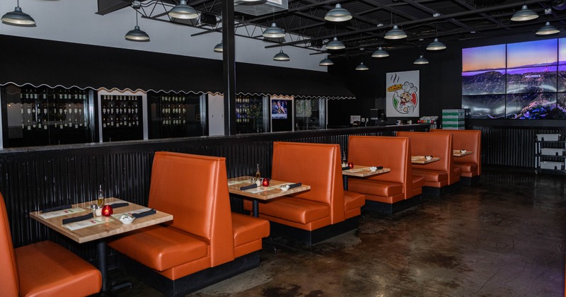 Interior of a restaurant with orange booths, concrete floors and pendant lights