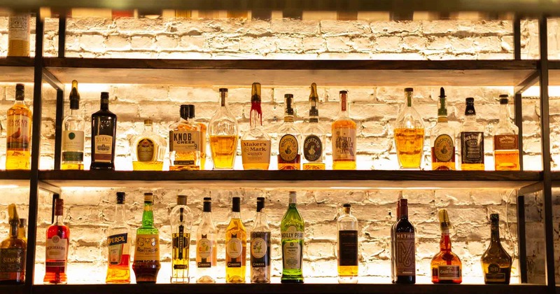 A shelf with bottle of drinks in front of the bar mirror.