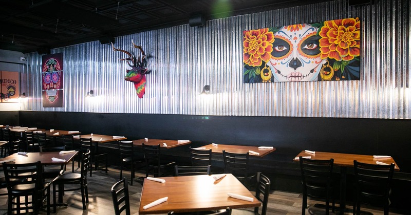 Interior, lined up tables and seating by a wall decorated with colorful artwork