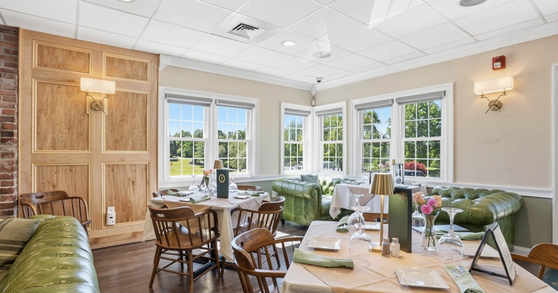 Dining area with wooden tables, green leather sofas, large windows, and scenic outdoor view