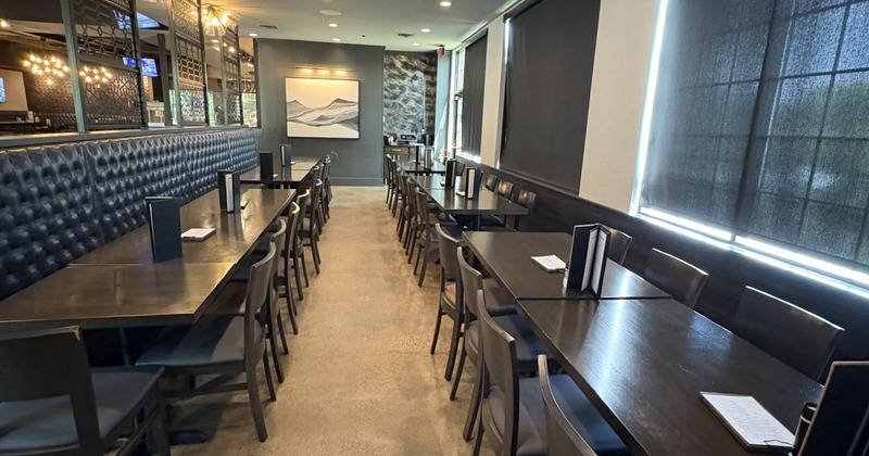 A room with long, dark wooden tables, chairs, and black upholstered booth seating
