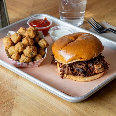 Smoked pulled pork sandwich served with BBQ sauce and tater tots.