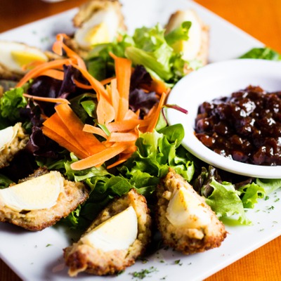 Scotch eggs quartered into slices on a plate with a green salad and a dish of pickled relish