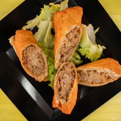 Cheesesteak Eggs Rolls served on a black plate over lettuce.