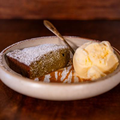 Matcha brownie with powdered sugar and miso caramel, served with a scoop of vanilla ice cream.