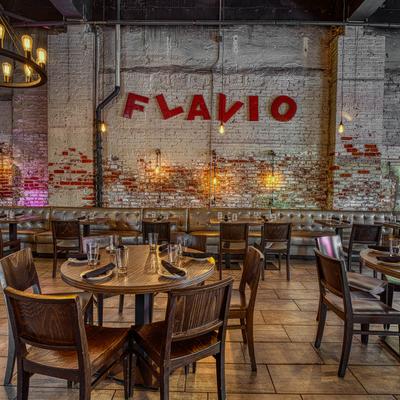 Interior with wooden tables and a red sign reading Flavio on a rustic wall.
