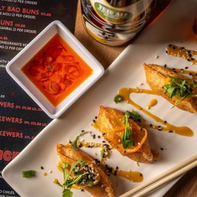 Philly cheese dumplings topped with sauce and sesame seeds, served with a dipping sauce.