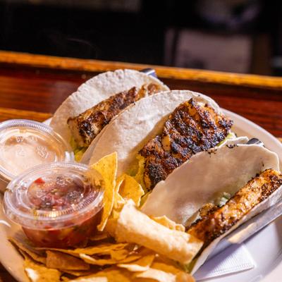 Fish tacos served with tortilla chips and two cups of dipping sauce.